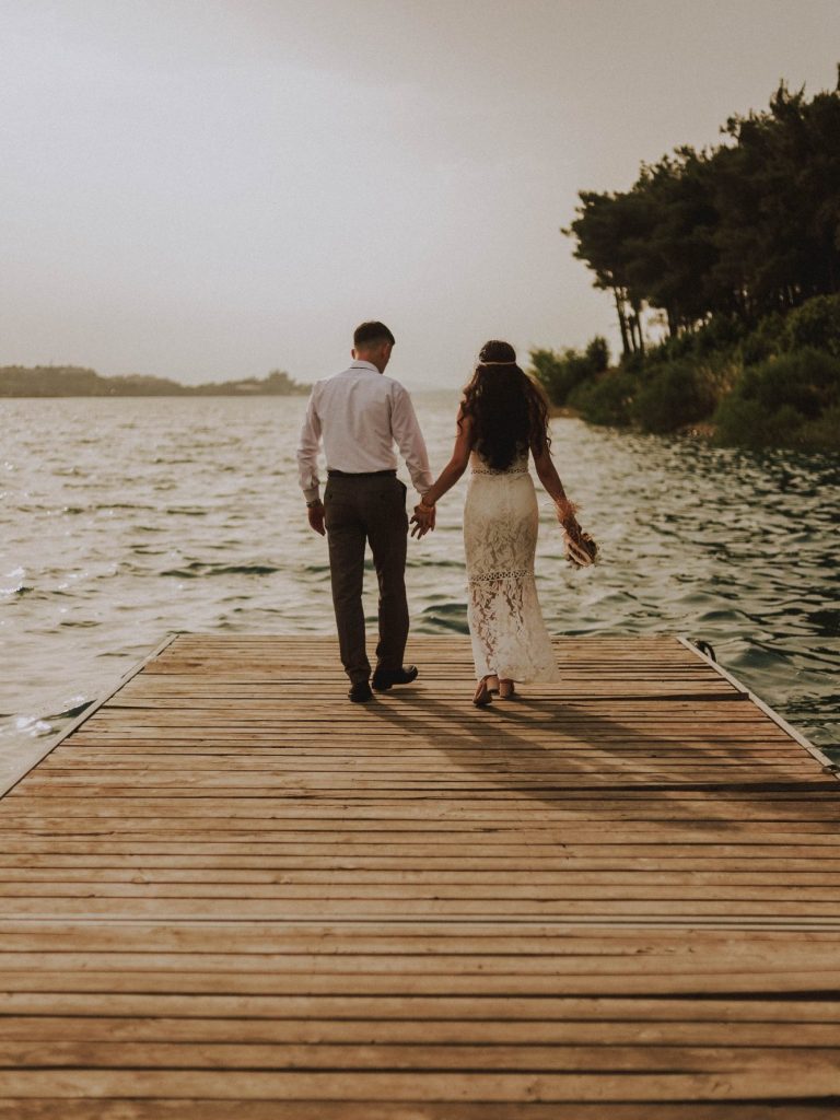 A couple walking along a pier, hand in hand and walking towards a lake